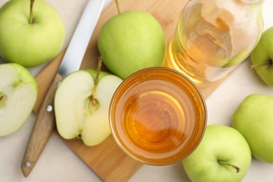 Photo of Fresh cider in glass, bottle, apples and knife on beige table, flat lay