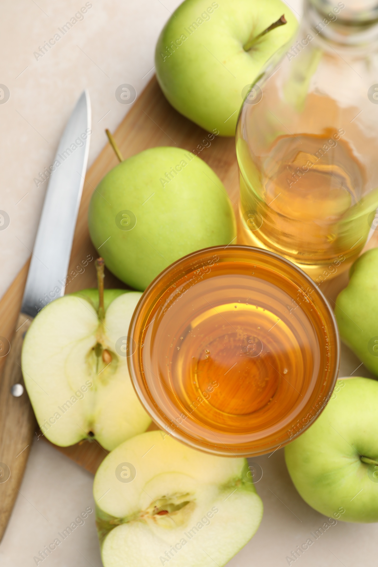 Photo of Fresh cider in glass, bottle, apples and knife on beige table, top view