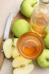 Photo of Fresh cider in glass, bottle, apples and knife on beige table, top view