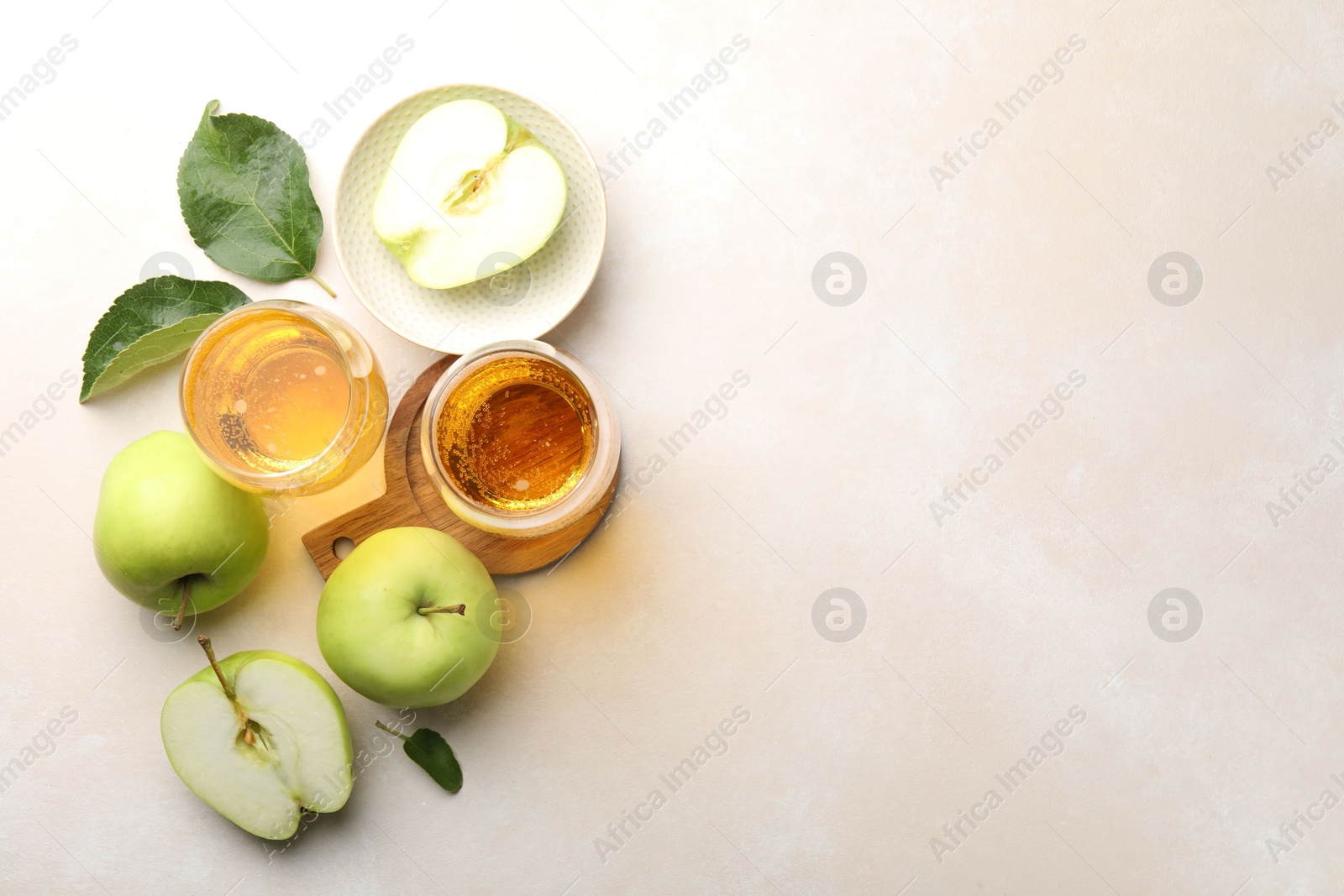 Photo of Fresh cider in glasses, apples and green leaves on beige table, flat lay. Space for text
