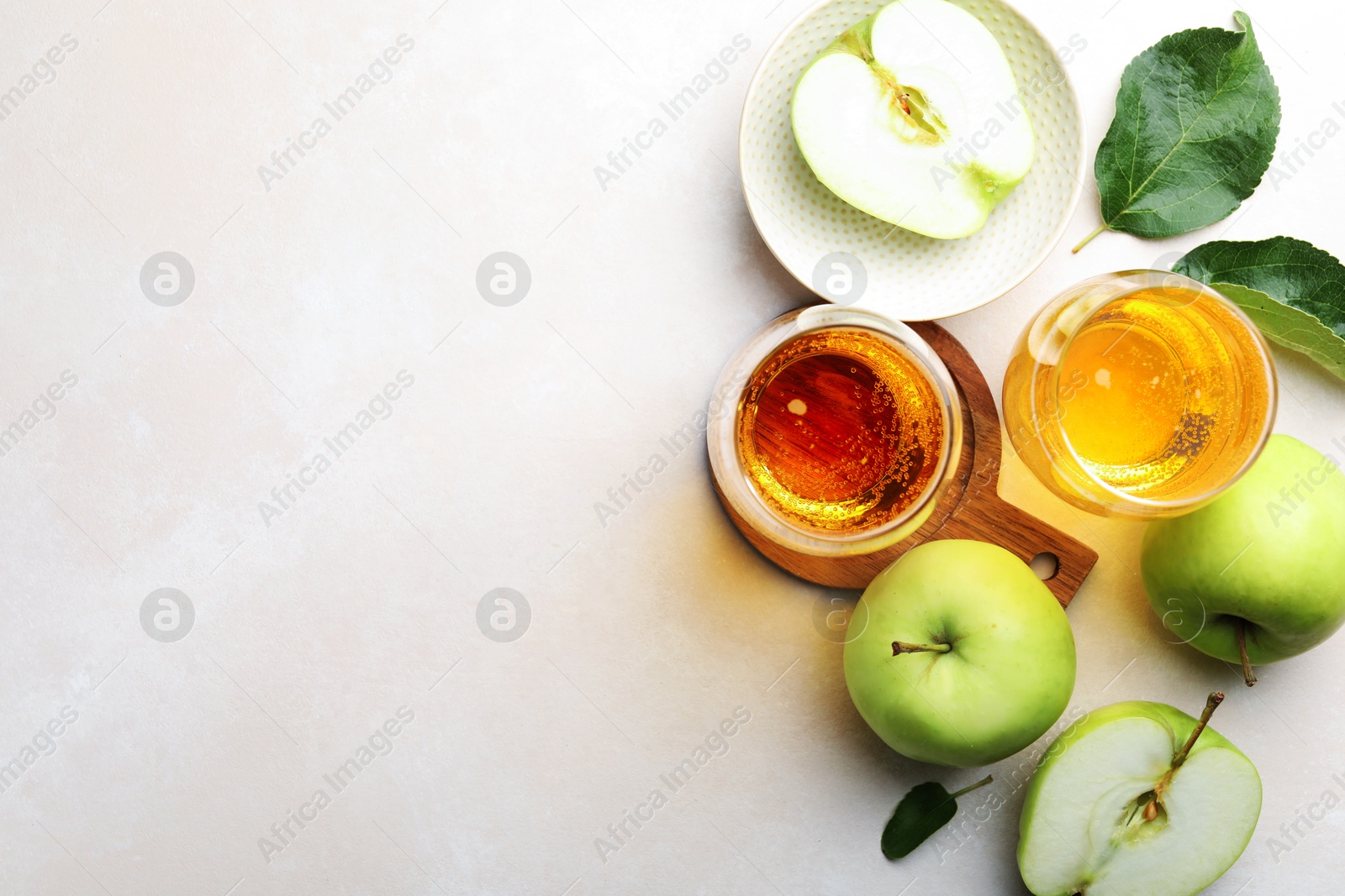 Photo of Fresh cider in glasses, apples and green leaves on beige table, flat lay. Space for text