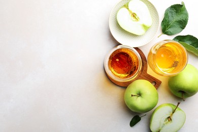 Photo of Fresh cider in glasses, apples and green leaves on beige table, flat lay. Space for text
