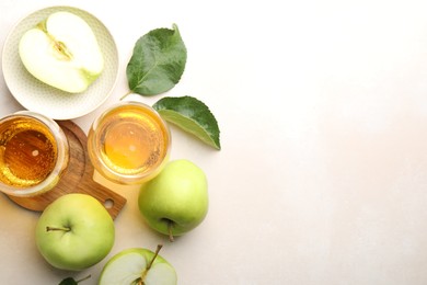 Photo of Fresh cider in glasses, apples and green leaves on beige table, flat lay. Space for text