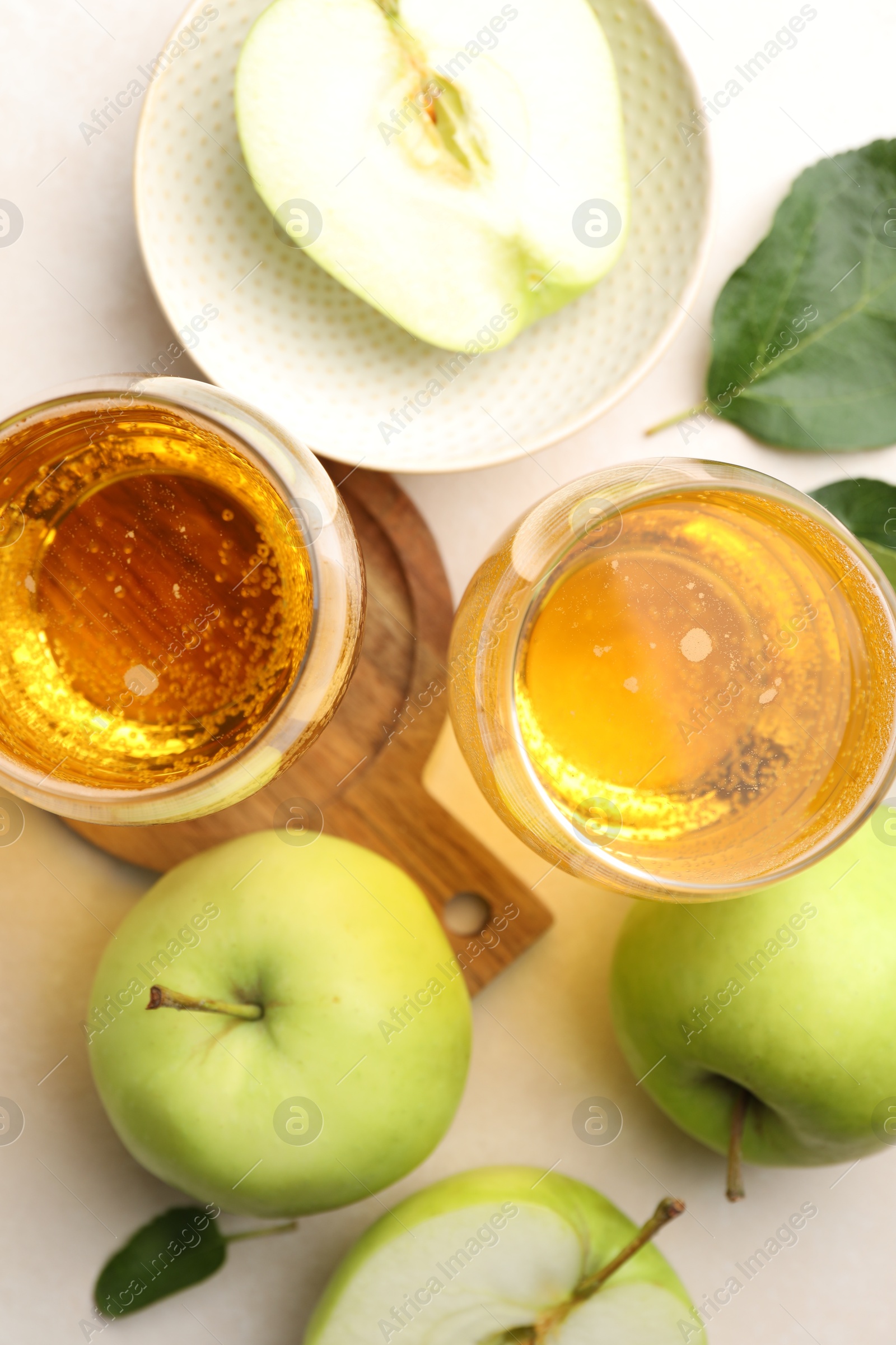 Photo of Fresh cider in glasses, apples and green leaves on beige table, flat lay