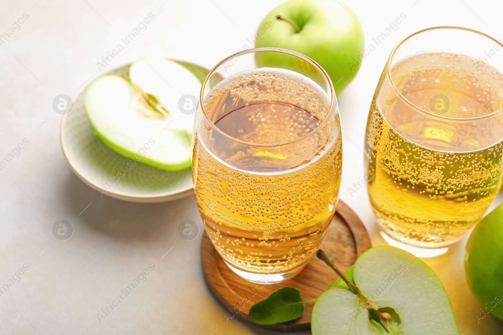 Fresh cider in glasses and apples on beige table, closeup Photo of Fresh cider in glasses and apples on beige table, closeup