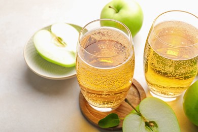 Photo of Fresh cider in glasses and apples on beige table, closeup