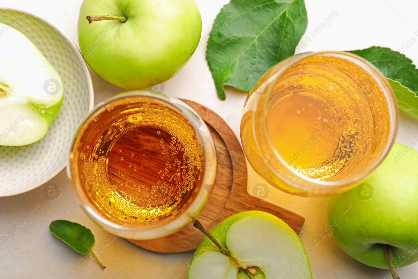 Photo of Fresh cider in glasses, apples and green leaves on beige table, flat lay