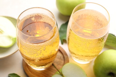 Photo of Fresh cider in glasses, apples and green leaves on beige table, closeup