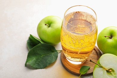 Photo of Fresh cider in glass and apples on beige table, closeup
