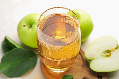 Photo of Fresh cider in glass and apples on beige table, closeup