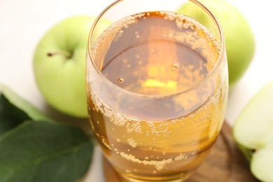 Photo of Fresh cider in glass and apples on beige table, closeup