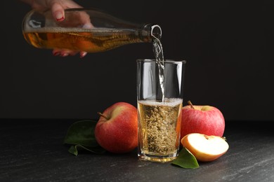 Photo of Woman pouring fresh cider into glass at black table, closeup