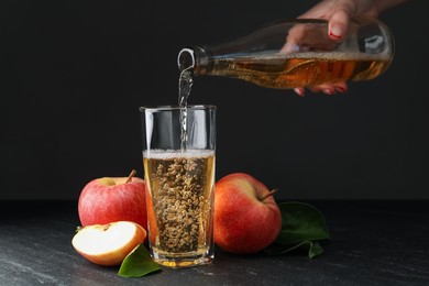 Photo of Woman pouring fresh cider into glass at black table, closeup