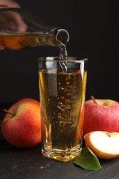 Photo of Woman pouring fresh cider into glass at black table, closeup