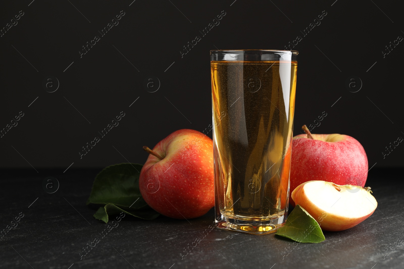 Photo of Fresh cider in glass, apples and green leaves on black table