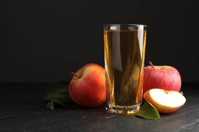 Photo of Fresh cider in glass, apples and green leaves on black table