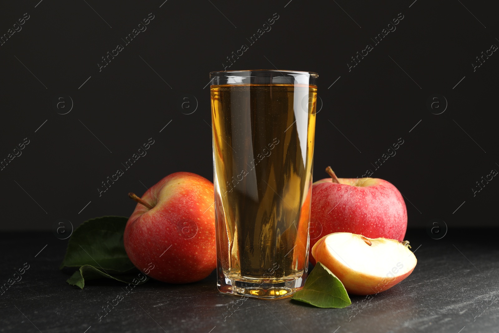 Photo of Fresh cider in glass, apples and green leaves on black table