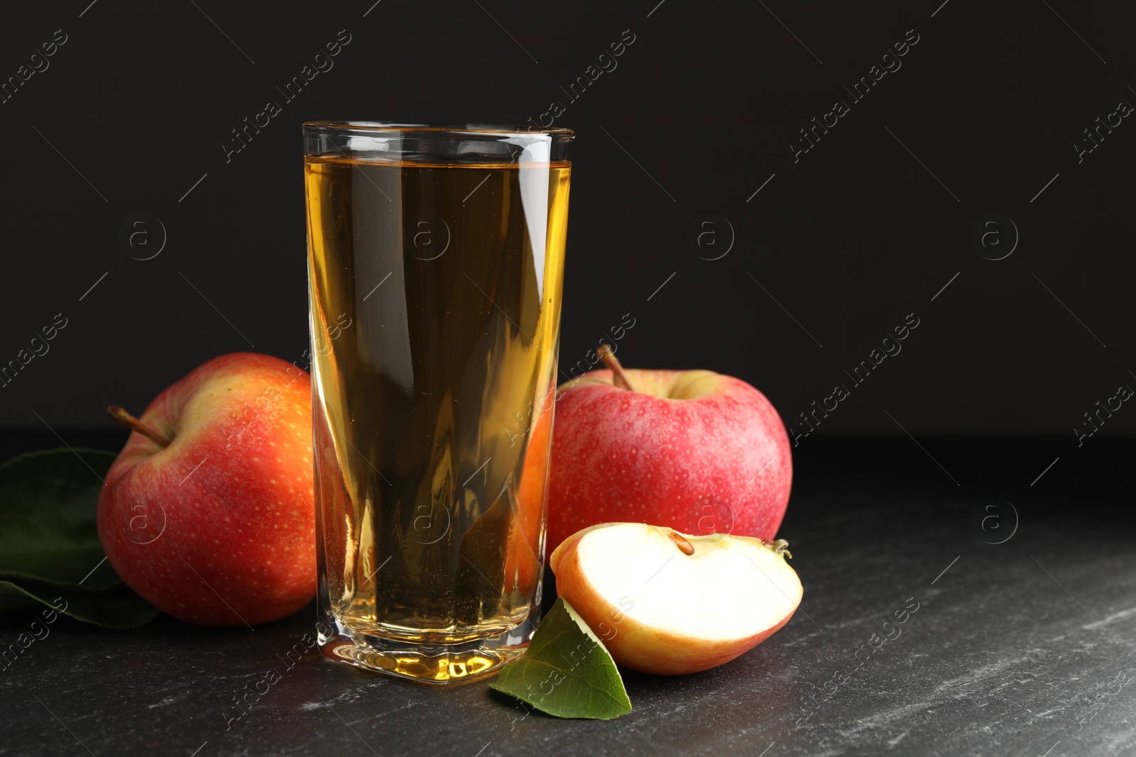 Photo of Fresh cider in glass, apples and green leaves on black table, space for text