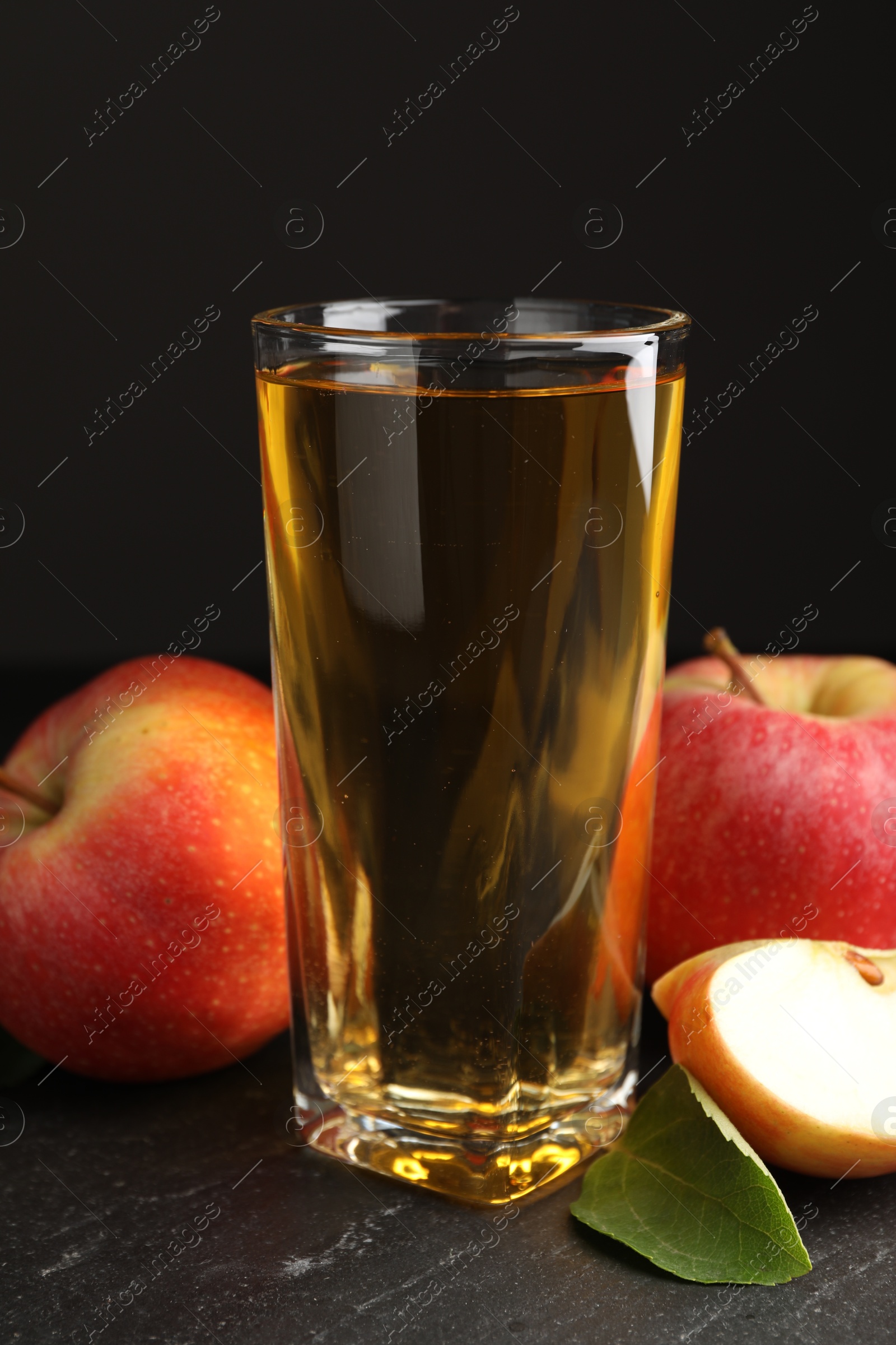 Photo of Fresh cider in glass, apples and green leaf on black table, closeup