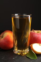 Photo of Fresh cider in glass, apples and green leaf on black table, closeup