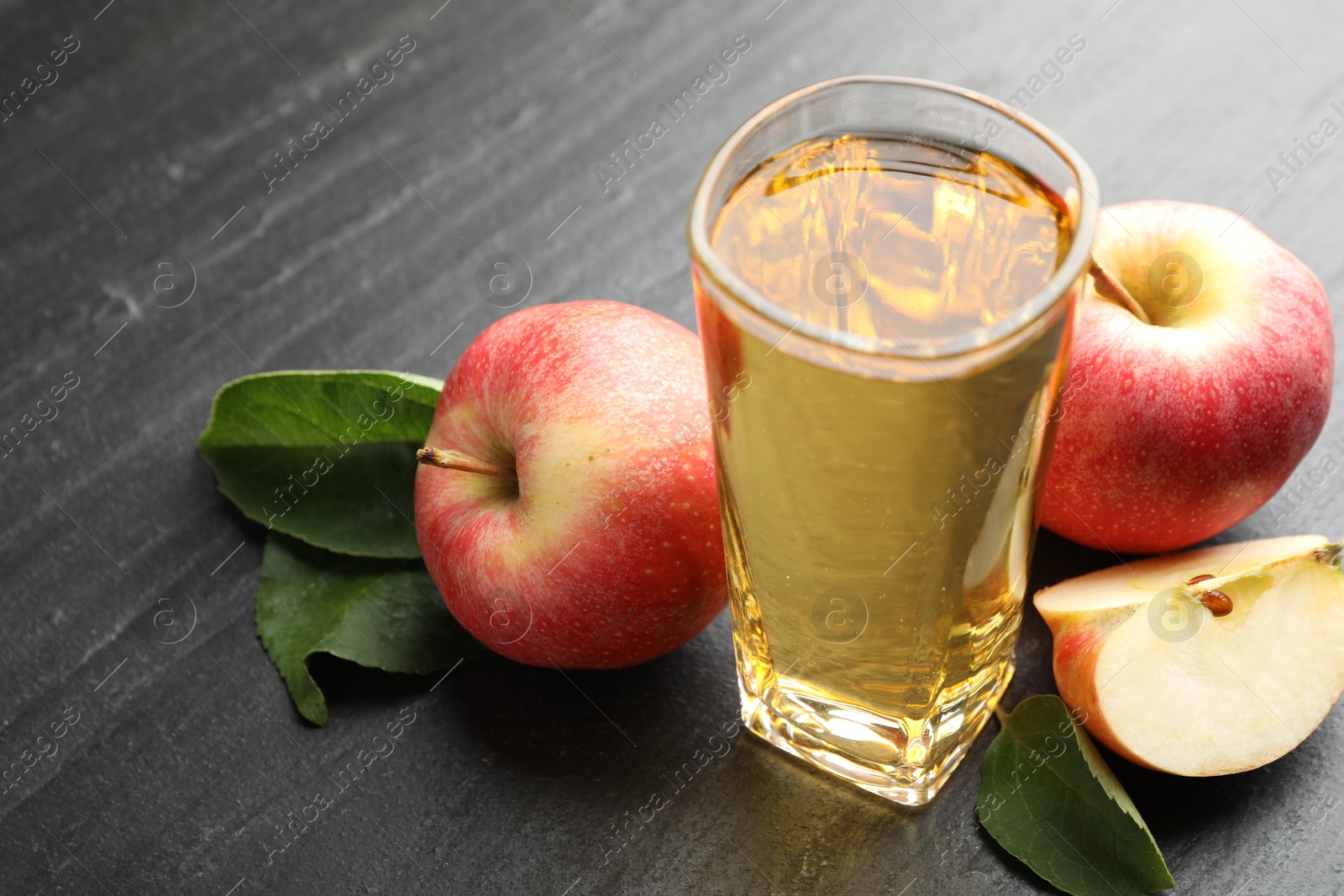 Photo of Fresh cider in glass, apples and green leaves on black table, closeup