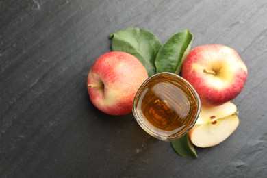 Photo of Fresh cider in glass, apples and green leaves on black table, flat lay. Space for text