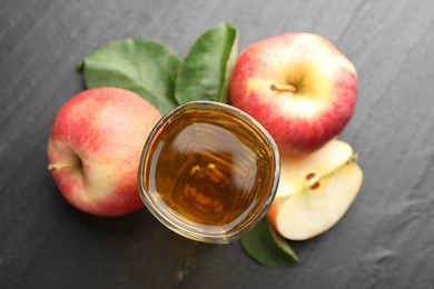 Photo of Fresh cider in glass, apples and green leaves on black table, flat lay