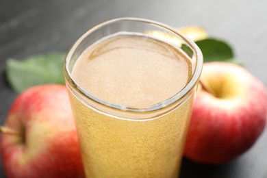 Photo of Fresh cider in glass and apples on black table, closeup