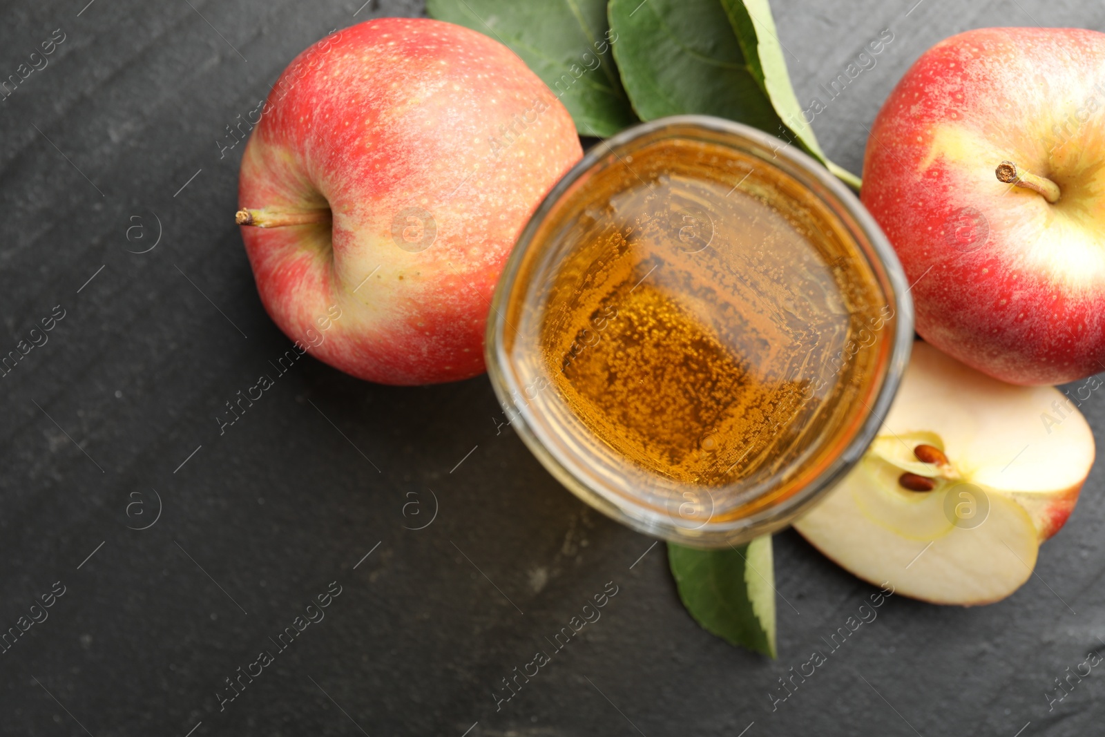 Photo of Fresh cider in glass, apples and green leaves on black table, flat lay. Space for text