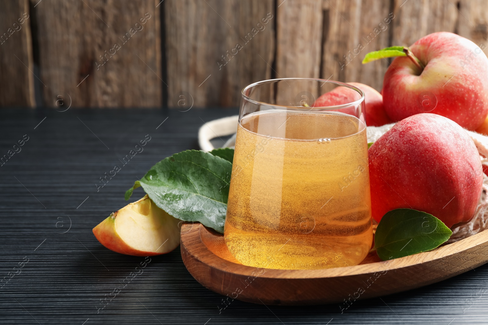 Photo of Fresh cider in glass, apples and green leaves on black textured table, closeup