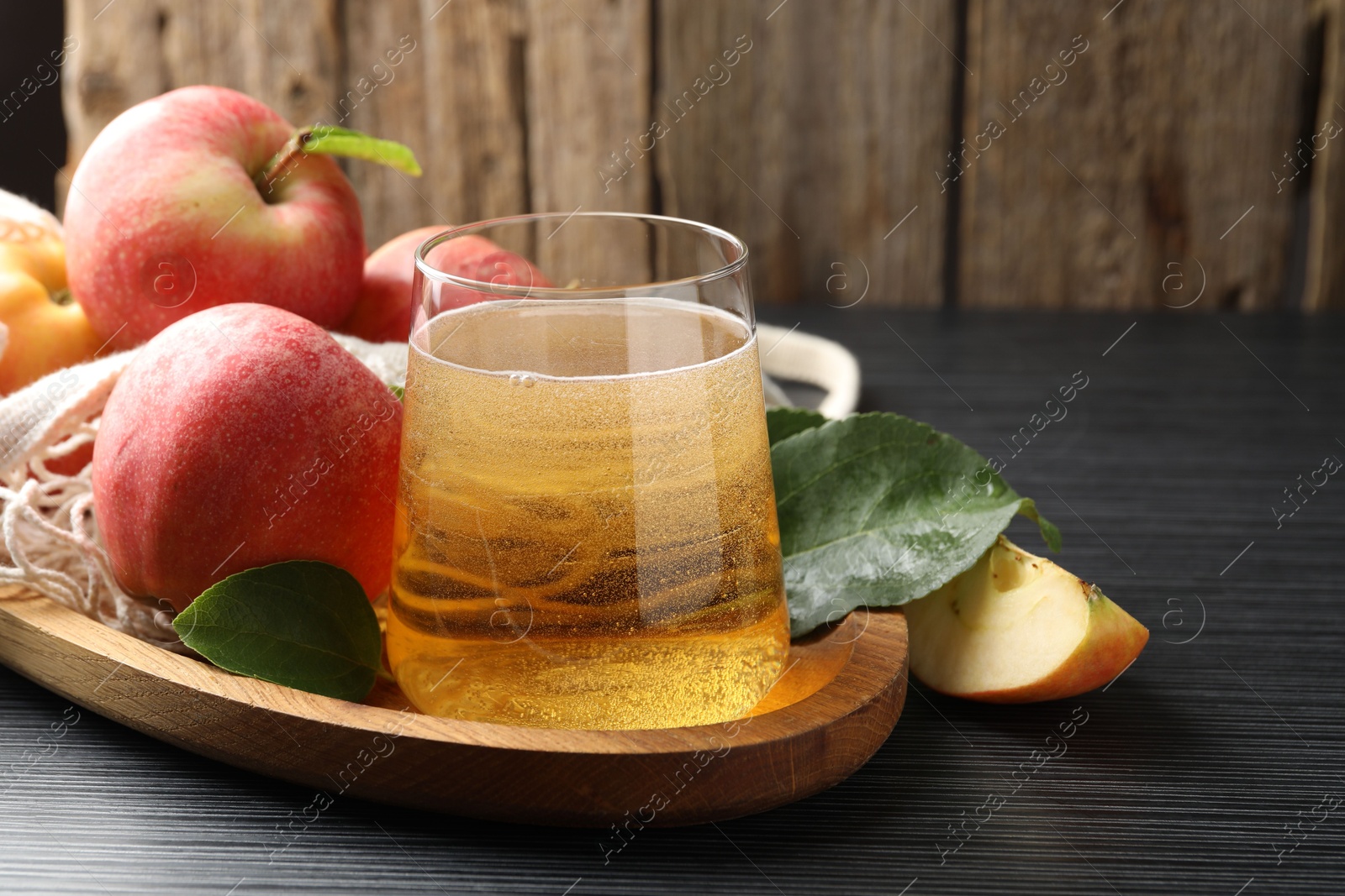 Photo of Fresh cider in glass, apples and green leaves on black textured table, closeup