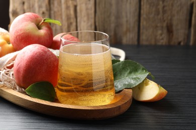 Photo of Fresh cider in glass, apples and green leaves on black textured table, closeup