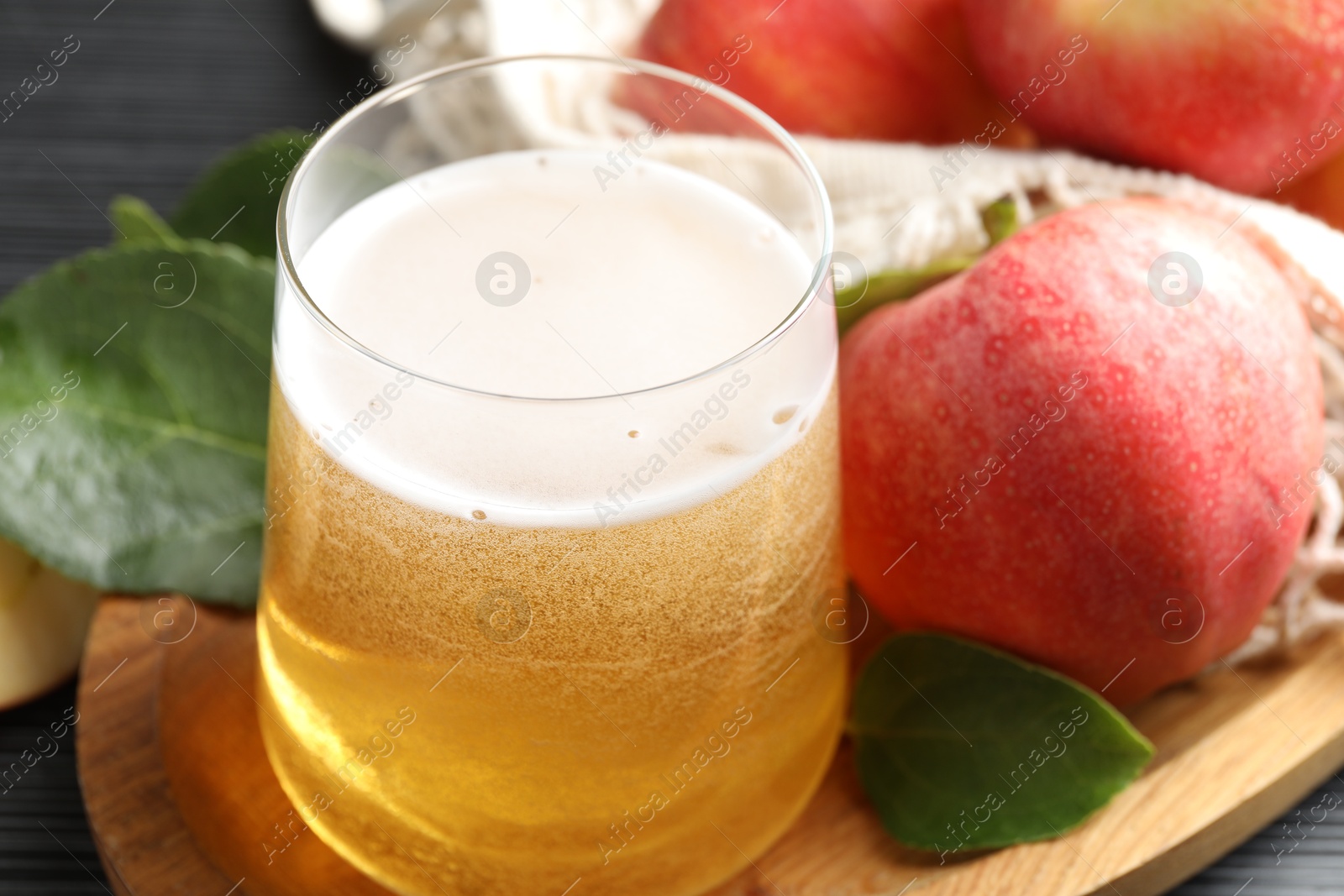 Photo of Fresh cider in glass, apples and green leaves on table, closeup
