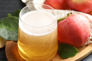 Photo of Fresh cider in glass, apples and green leaves on table, closeup