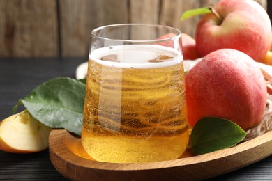 Photo of Fresh cider in glass, apples and green leaves on black textured table, closeup