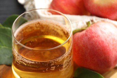 Photo of Fresh cider in glass, apples and green leaves on table, closeup