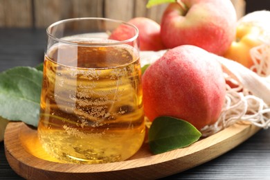 Photo of Fresh cider in glass, apples and green leaves on table, closeup