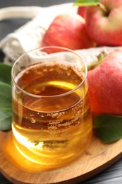 Photo of Fresh cider in glass, apples and green leaves on table, closeup