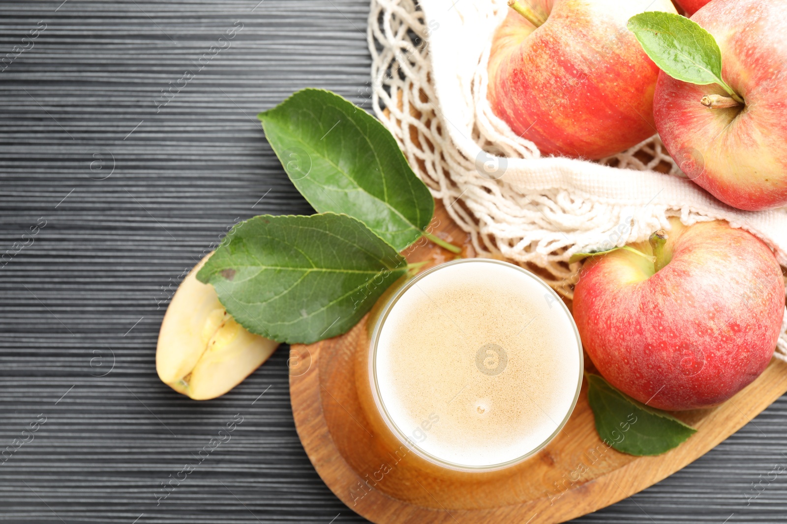 Fresh cider in glass, apples and green leaves on black textured table, flat lay Photo of Fresh cider in glass, apples and green leaves on black textured table, flat lay