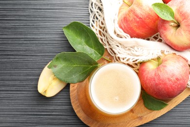 Photo of Fresh cider in glass, apples and green leaves on black textured table, flat lay