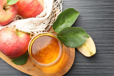 Photo of Fresh cider in glass, apples and green leaves on black textured table, flat lay