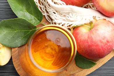Photo of Fresh cider in glass, apples and green leaves on black textured table, flat lay