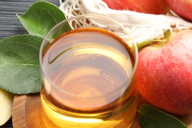 Photo of Fresh cider in glass, apples and green leaves on table, closeup