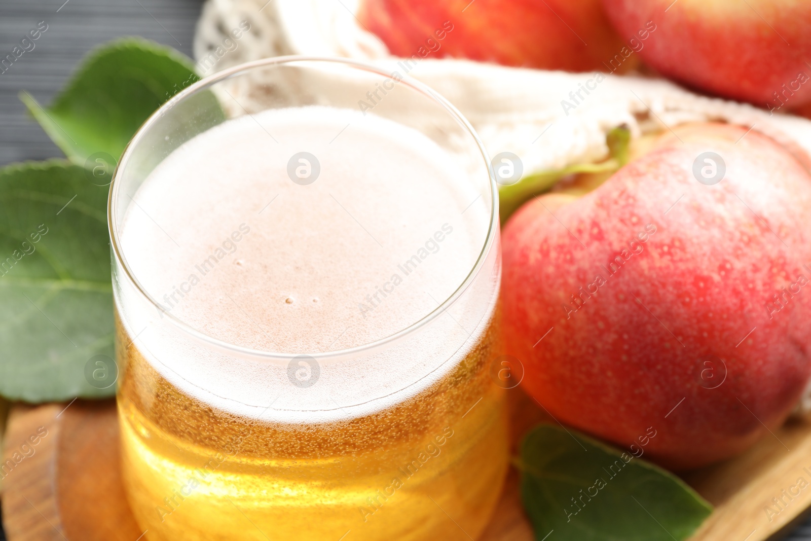 Photo of Fresh cider in glass, apples and green leaves on table, closeup