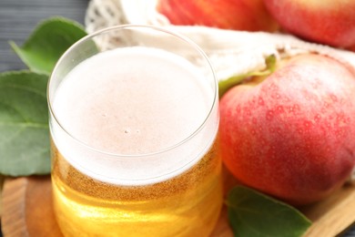 Photo of Fresh cider in glass, apples and green leaves on table, closeup