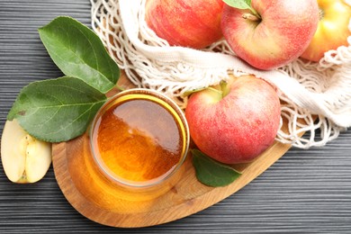 Photo of Fresh cider in glass, apples and green leaves on black textured table, flat lay