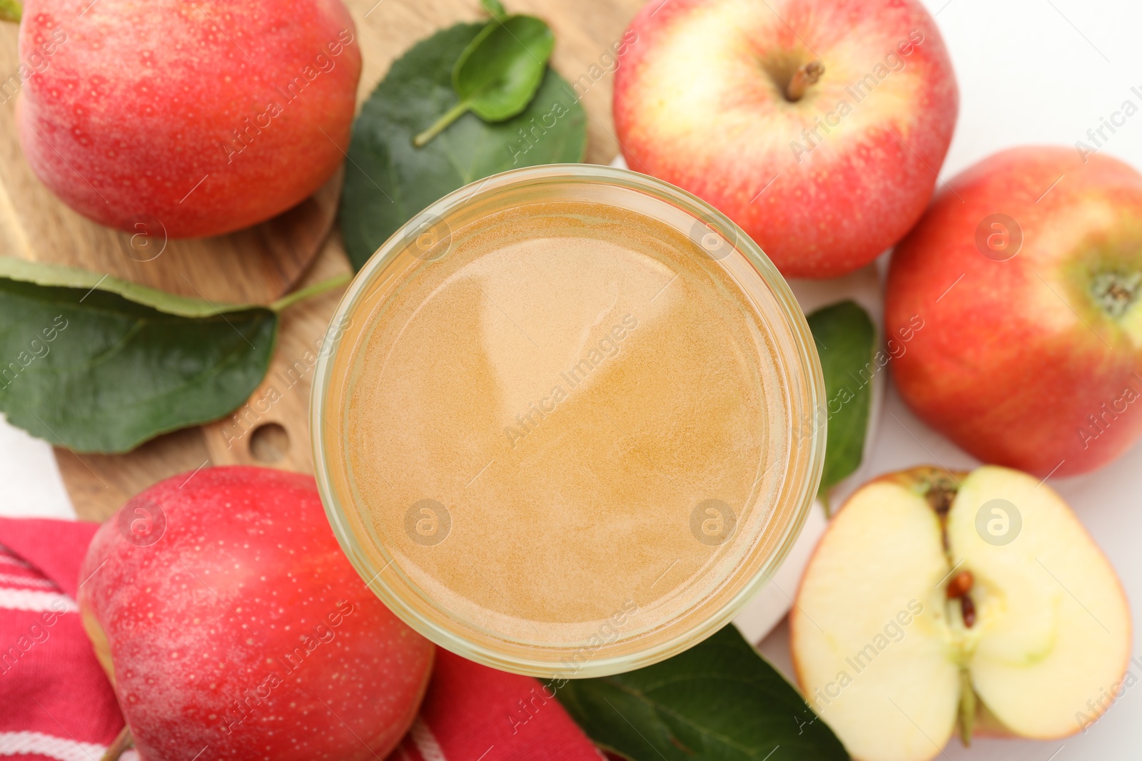 Fresh cider in glass, apples and green leaves on white table, flat lay Photo of Fresh cider in glass, apples and green leaves on white table, flat lay