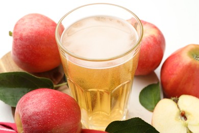 Photo of Fresh cider in glass and apples on white table, closeup