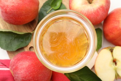 Photo of Fresh cider in glass, apples and green leaves on table, flat lay