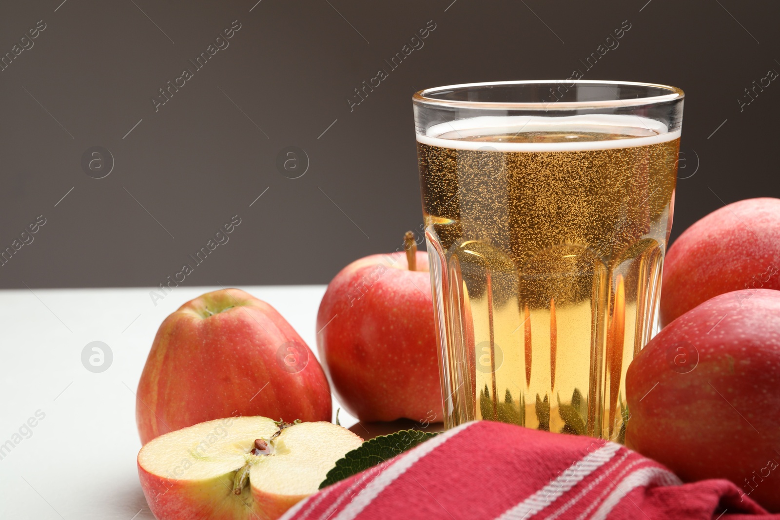 Fresh cider in glass and apples on white table, closeup Photo of Fresh cider in glass and apples on white table, closeup
